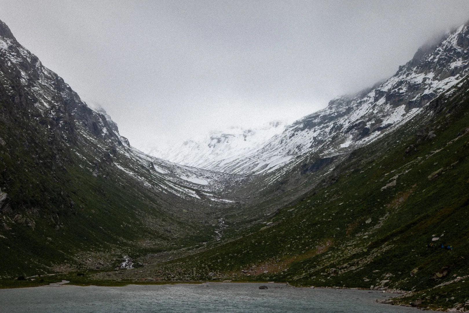Fine art photography High Tauern II by Ziggy Kańczukowski capturing a valley with snow-capped mountains and a lake under a cloudy sky.