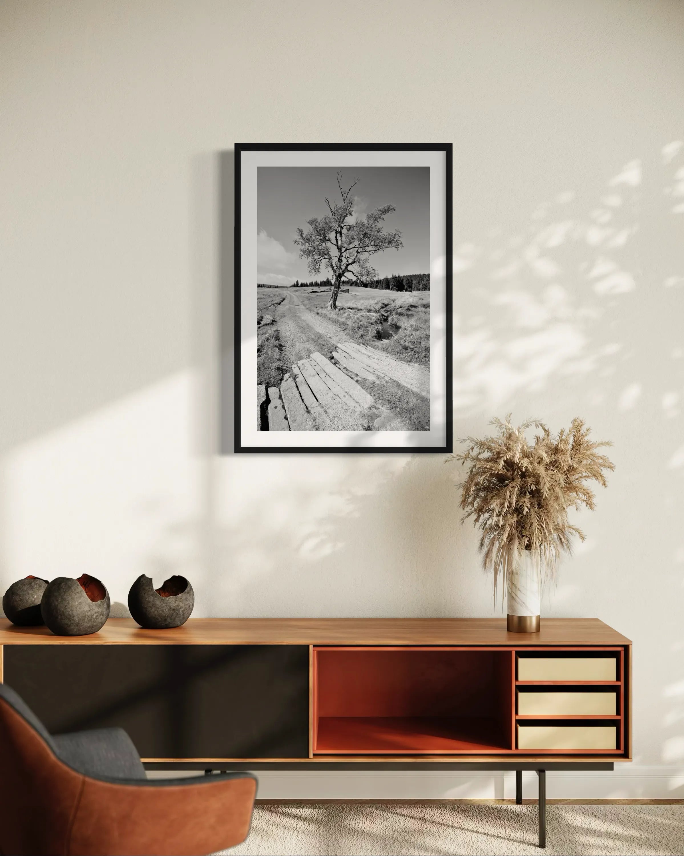 Framed black and white fine art landscape print Izera Meadow by Ziggy Kańczukowski displayed on a wall above a wooden cabinet with decorative items.