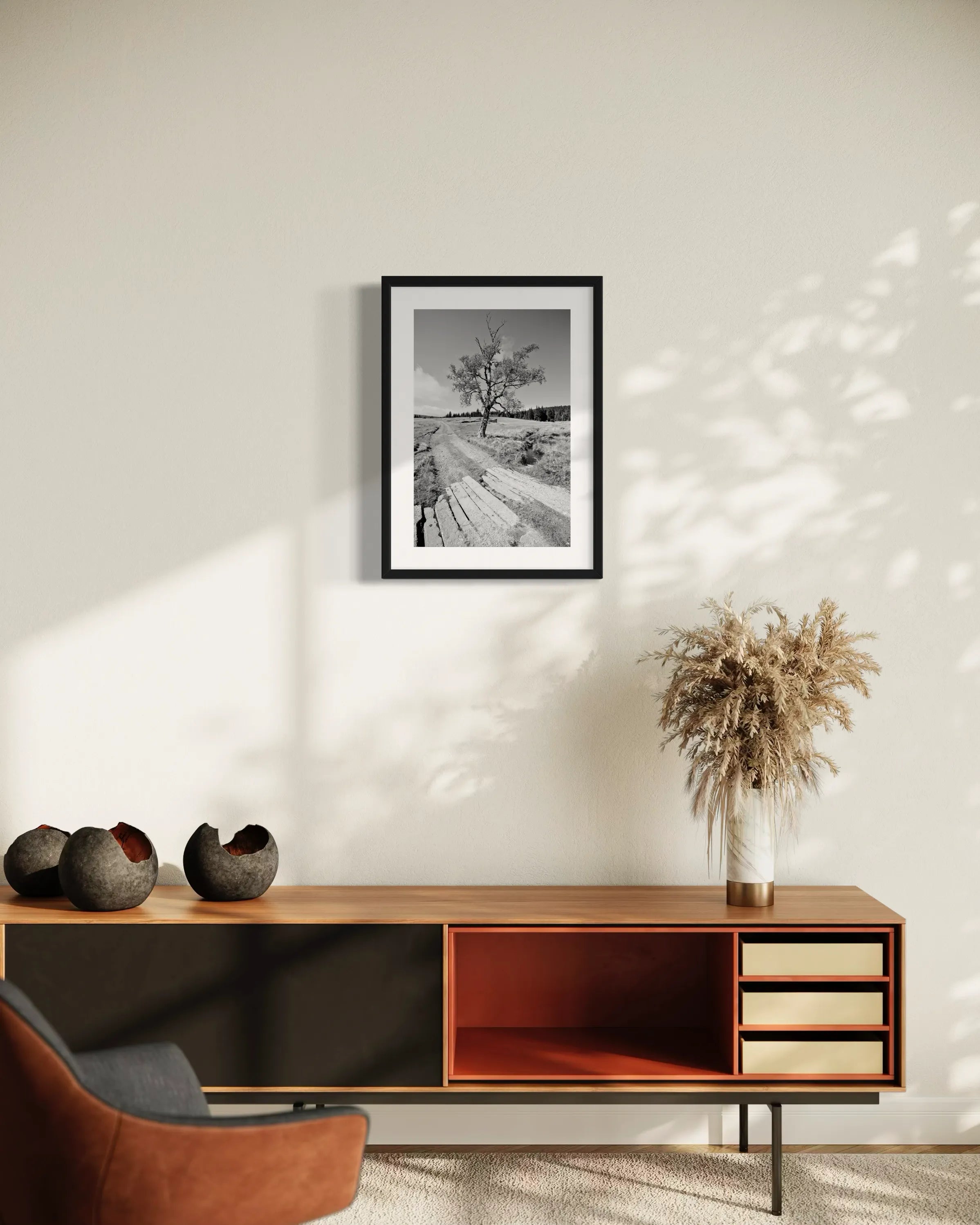 Framed black and white fine art landscape print Izera Meadow by Ziggy Kańczukowski displayed on a wall above a wooden cabinet with decorative items.