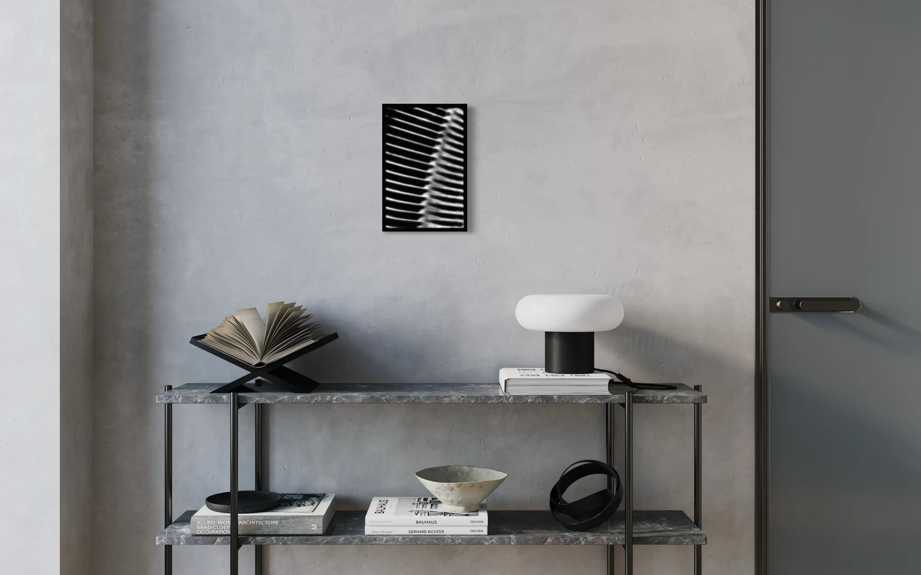 Framed black and white fine art print Machine 02 by Ziggy Kańczukowski displayed on a shelf with books and a lamp against a gray wall in a modern interior.