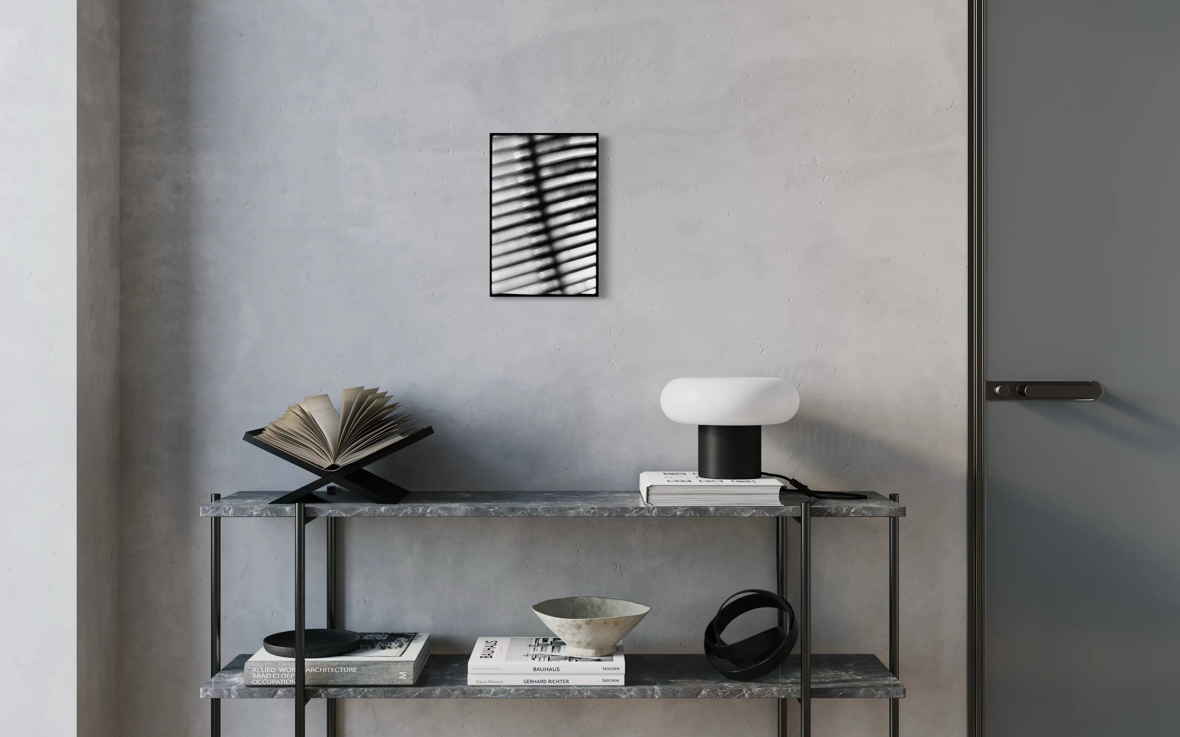 Framed black and white fine art print Machine 04 by Ziggy Kańczukowski displayed on a shelf with books, a bowl, and a lamp against a gray wall in a modern interior.