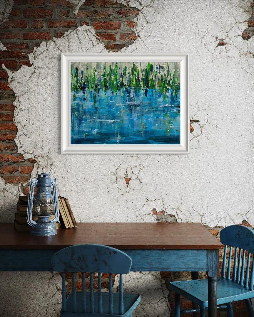 Framed abstract painting Pond by Oliwia Tomczak hanging on a textured wall above a wooden table and blue chairs.